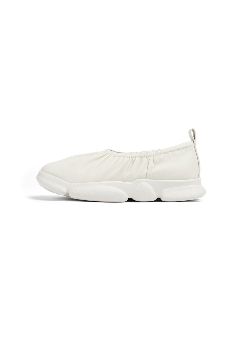 Bílé slip-on boty s nařaseným textilním svrškem a flexibilní podrážkou s texturovaným vzorem. Kulatá špička a poutko na zadní straně.