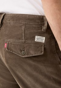 Pantaloni in velluto a coste marroni con righe verticali, dotati di un taschino sul retro con una patta e un bottone, e un'etichetta Levi's.