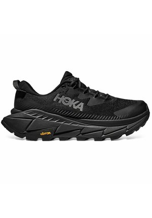 Chaussure de course noire HOKA avec semelle épaisse, lacets et logo Vibram grip sur le bord extérieur de la semelle.