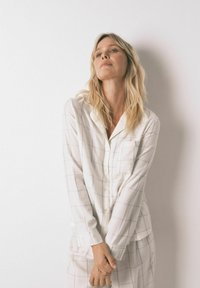 Hvidternet pyjamas sæt lavet af blødt stof, med en skjorte med knaplukning og lomme samt afslappede bukser.