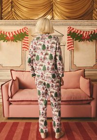 Pižama set v prazničnem slogu z roza ozadjem, zelenimi drevesi in prazničnimi ilustracijami. Mehka tkanina; sproščen kroj; v kombinaciji z bež nogavicami.