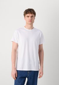 Hvit bomullst-skjorte med korte ermer og rund hals, med en avslappet passform og jevn, glatt tekstur. Brukt sammen med blå jeans.
