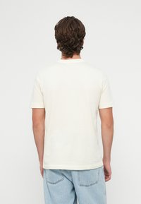 Kremowa koszulka z krótkim rękawem i okrągłym dekoltem, wykonana z miękkiej bawełny, z gładkim tyłem i luźnym krojem.