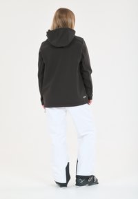 Veste imperméable noire avec capuche, associée à un pantalon blanc avec des accents noirs, vue de l'arrière. Tissu lisse et durable.