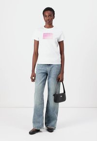 T-shirt en coton blanc avec un imprimé graphique rose, associé à un pantalon en jean large bleu clair et un petit sac à main noir. Chaussures noires à enfiler.