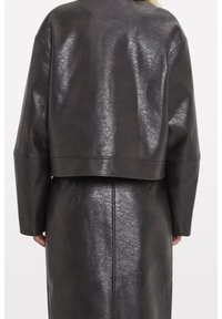 Svart läderliknande jacka med en något strukturerad yta. Har en kortad design och sänkta axlar, med en ren, minimalistisk silhuett.