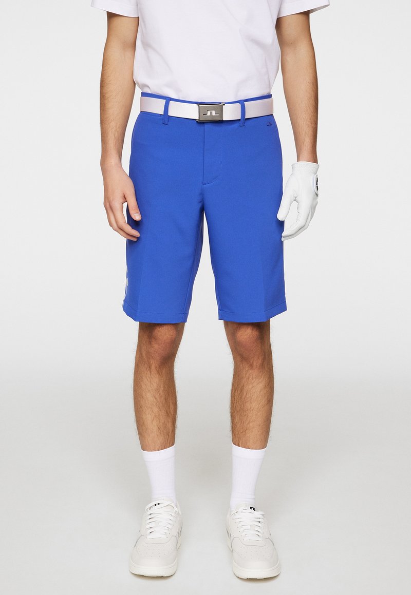 Niebieskie szorty golfowe o gładkiej fakturze, z płaskim przodem i prostym krojem. Połączone z białym paskiem, białą koszulą i białymi trampkami.