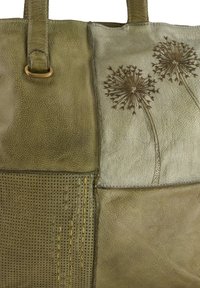 Olijfgroene leren tas met gek textureerde delen, geperforeerde details en gegraveerde paardenbloem ontwerpen.