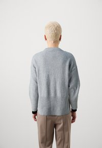 Grau gestrickter Pullover aus Wolle mit geripptem Saum, überlangen Schultern und langen Ärmeln. Glatte Textur mit einem kontrastierenden schwarzen inneren Bündchen.
