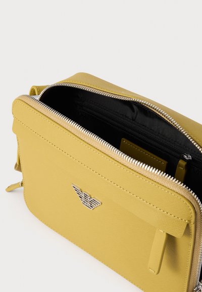 Yellow leather crossbody bag with silver logo and open zipper showing black interior and inner zippered pocket.