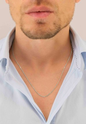 Silberne Kettenhalskette ruht auf einem nackten Hals, getragen mit einem hellblauen Hemd mit offenem Kragen. Glatte Textur mit dezentem Glanz.