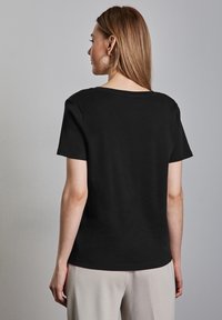 Černé tričko s krátkým rukávem a kulatým výstřihem, z hladké látky, viděné ze zadní strany. Má mírnou elastčnost a uvolněný střih.