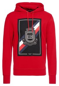 Sudadera roja con panel frontal negro que presenta rayas diagonales blancas, marinas y rojas, y un emblema con las iniciales "TH", además de cordones ajustables.