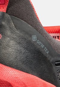 Čierna a červená športová obuv s textúrovaným povrchom, značením GORE-TEX a gumovou pätou pre odolnosť a podporu.