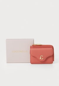 Korallefarbene Lederbörse mit strukturiertem Finish, Klappe an der Vorderseite, goldfeinem Logo-Akzent und Reißverschluss; präsentiert in einer rosa gebrandeten Schachtel.