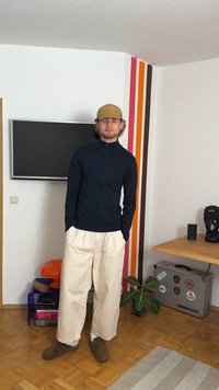 Giacca leggera blu navy con zip, pantaloni beige a gamba larga, pantofole marroni, in piedi di fronte a strisce colorate su un muro, decorazione moderna.