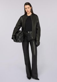 Giubbotto bomber in pelle nera con colletto a costine, top aderente nero, pantaloni in pelle a vita alta, guanti neri e borsa nera con texture.
