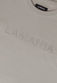 Light gray cotton t-shirt featuring raised, embroidered text "LAMANIA" across the front. Round neckline with stitching details.