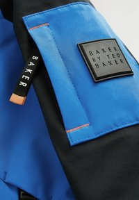 Niebieska i czarna kurtka z gładkiego materiału, z kontrastowymi szwami i prostokątną naszywką z logo "BAKER BY TED BAKER."