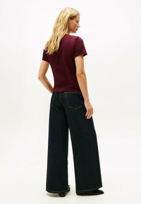 Bordeaux t-shirt med korte ærmer, parret med mørkeblå vide jeans. Glat tekstur med kontrasterende syninger.