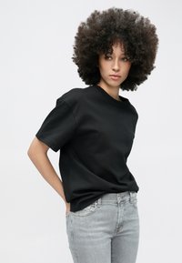 Tricou negru cu mâneci scurte, din bumbac, cu croială lejeră și decolteu rotund, asortat cu blugi mulați de culoare gri deschis.