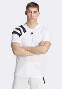 Hvid atletisk t-shirt med sorte diagonale striber på venstre skulder, med en v-halsudskæring og en struktureret overflade for åndbarhed.