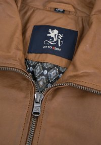 Braune Lederjacke mit einem silbernen Reißverschluss, ausgestattet mit einem schwarz-weißen gemusterten Innenfutter. Etikett lautet "OTTO KERN." Strukturierte Oberfläche.
