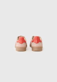 Footwear with a smooth coral leather heel and light pink suede upper, featuring a textured tan rubber sole and subtle logo detail.