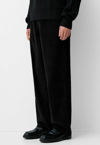 Black corduroy trousers with a straight fit, featuring textured fabric and side pockets, paired with black loafers.