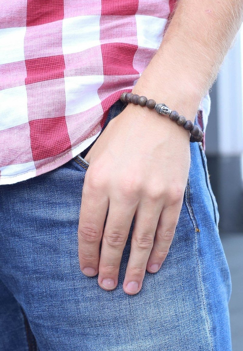 Donkerhouten kralenarmband met een zilveren Boeddha-bedel. Hand rustend op denim met een lichtblauwe wassing en een rood-wit geruite shirt erboven.