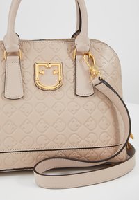 Sac à main en cuir beige avec motif géométrique embossé, fermoir logo doré, double poignées et bandoulière amovible.