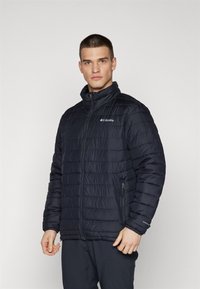 Giacca puffer di un blu navy scuro con colletto alto, apertura frontale con zip, design a trapunta a fantasia e logo sul lato sinistro del petto. Presenta tasche laterali.