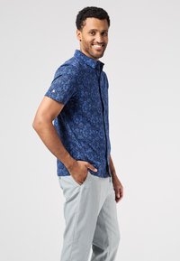 Camisa de manga corta en azul marino con un patrón floral, que cuenta con un cuello moderno y un corte relajado, combinada con pantalones gris claro.