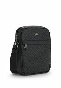 Black crossbody bag with a geometric pattern, zip closure, silver hardware, and an adjustable strap. Logo displayed on the front.