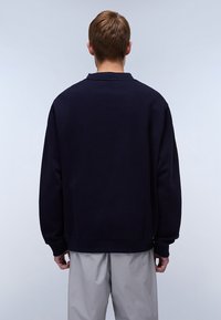 Diepblauwe sweatshirt met een ronde hals, ribgebreide manchetten en zoom, met een ontspannen pasvorm en zachte textuur. De achtergrond is lichtgrijs.