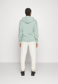 Mint green hoodie with a drawstring and ribbed cuffs, paired with cream joggers. Black sneakers with a textured design complete the look.