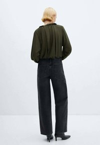 Bluză verde-oliv cu detalii strânse la spate, asortată cu blugi negri, cu talie înaltă și croi lejer, și pantofi cu toc ascuțit negri.