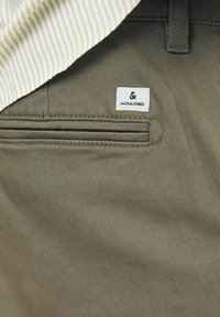 Oliven grønne bukser med et elegant design, der har en baglomme og et hvidt mærke med "JACK&JONES" i sort tekst.