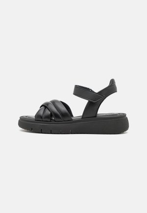 Schwarze Leder-Sandalen mit überkreuzten Riemen, verstellbarem Knöchelriemen und einer dicken, strukturierten schwarzen Sohle. Minimalistisches Design ohne Verzierungen.
