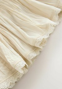 Tessuto plissettato color crema con rifiniture in pizzo intricate lungo i bordi, drappeggiato delicatamente su una superficie chiara.