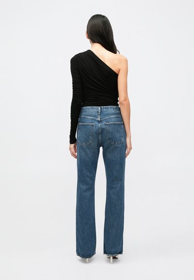 Μαύρο ασύμμετρο μακρυμάνικο τοπ με ριγέ υφή, συνδυασμένο με ψηλόμεσα μπλε τζιν παντελόνια με πίσω τσέπες και ίσια γραμμή ποδιού.