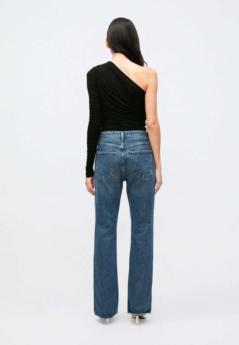 Haut noir asymétrique à manches longues avec texture froncée, associé à un jean bleu taille haute avec poches arrière et coupe droite.