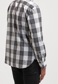 Camicia a quadri bianco e nero con maniche lunghe, polsini con bottoni e orlo curvo. Realizzata in tessuto leggero con una consistenza liscia.