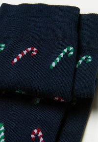 Marineblå sokker med slikstokkemønster i rød, grøn og hvid. Lavet af et blødt, textured strikstof. Foldet øverst.