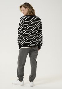 Black and white zigzag patterned sweater, relaxed fit, long sleeves, paired with gray tapered pants and white sneakers.