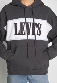 Felpa grigia con un pannello bianco e un grande logo nero "LEVI'S", con coulisse regolabile e tasca anteriore a marsupio.