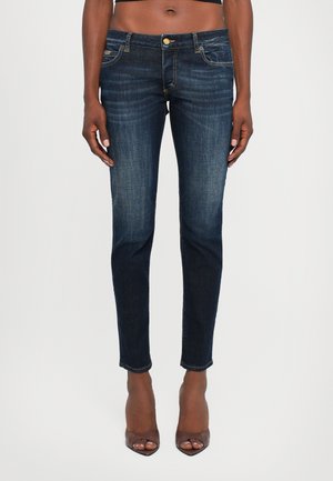 Tumed sinine denim skinny-jesid kerge pleekimisega, viie taskuga, kuldse nööbiga ja pahkluuni ulatuva servaga. Sujuv tekstuur ja keha järgiv disain.
