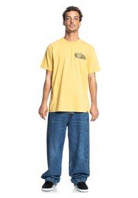 Losse gele katoenen t-shirt met een grafisch ontwerp op de borst. Gecombineerd met oversized blauwe denim jeans en zwarte instappers.