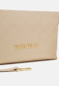 Pochette matelassée beige avec logo Valentino doré et bracelet assorti avec ferrures dorées et nom de la marque gravé.