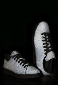 Zapatillas blancas con un patrón texturizado de escamas de pez, cordones negros y suelas de goma. El diseño incluye una punta redondeada y un perfil bajo.